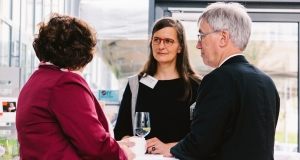 Im Gespräch an einem Stehtisch stehen links von hinten zu sehen Sabine Riewenherm (links), Präsidentin des BfN mit einem roten Jackett, in der Mitte Dr. Petra Dieker, die neue Leitung des Monitoringzentrums in einem schwarzen Kleid, mit langen hellbraunen glatten Haaren und einer roten Brille, rechts neben ihr von der Seite, Dr. Andreas Krüß in einem schwarzen Jackett, mit grau melierten Haaren und einer Brille.  