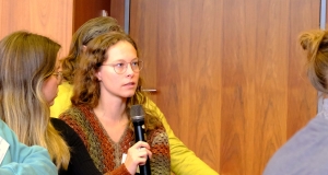 Eine Frau sitzt im Publikum und spricht in ein Mikrofon