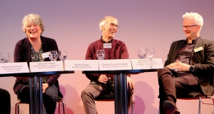 Eine Frau und zwei Männer sitzen zusammen auf der Bühne und lachen herzlich während der Podiumsdiskussion 