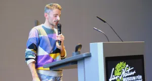 Ein Mann steht hintern einem Pult und hält einen Vortrag