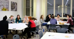 Einige Menschen sitzen um zwei Tische, auf deinen große Plakate liegen. Sie diskutieren und schreiben auf die Plakate.