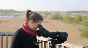 Eine Frau schaut durch ein schwarzes Spektiv. 