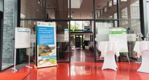 Eingangsbereich des Veranstaltungsorts mit Informationsmaterial, Roll-up und Stehtischen