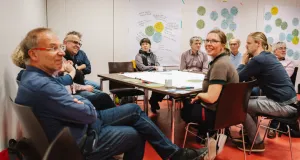 Teilnehmende sitzen in einem Workshop-Raum in kleiner Runde um einen Tisch und diskutieren konzentriert. Auf dem Tisch liegen Notizen und Arbeitsblätter – gemeinsam wird an der Beschreibung von Datenportalen gearbeitet.