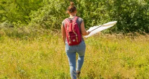 A woman walking across a green meadow with tall grass, carrying a large net.