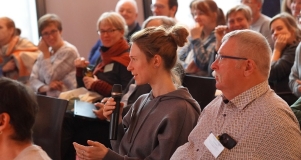 Eine Frau sitz im Publikum und hält Mikrofon in der Hand, um eine Frage zu stellen