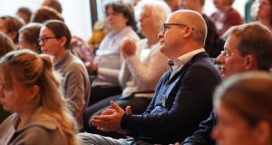 Das Publikum applaudiert. im Zentrum des Bildes ist ein Mann fokussiert, der Rest des Publikums um ihn herum ist unscharf.