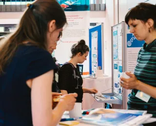 Drei Teilnehmerinnen im Gespräch am Informationsstand des Monitoringzentrums auf dem 2. Forum.