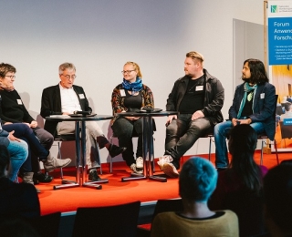 Seven people sit in a semicircle on the podium and discuss.